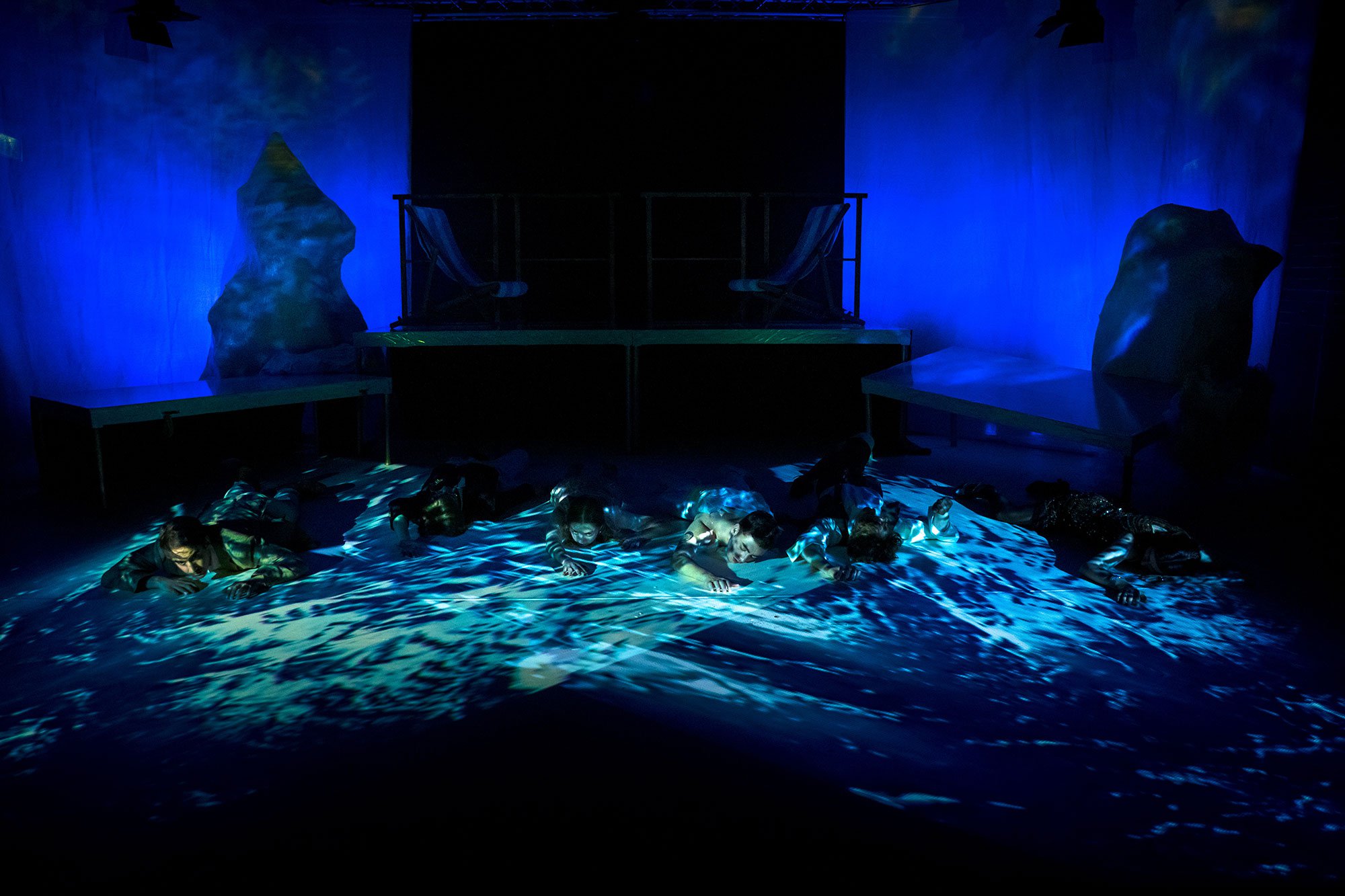 Six people float in a projection of water, with an iceberg and ruins of a boat around them